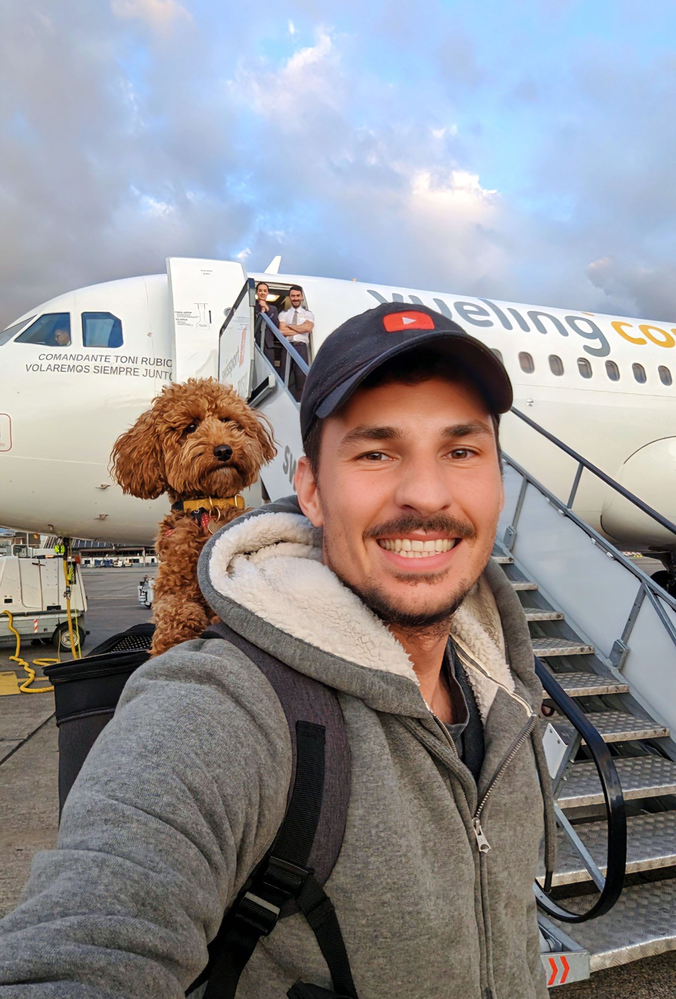 Tadej taking a selfie on the airport tarmac with Lex the poodle in a backpack carrier, boarding a plane